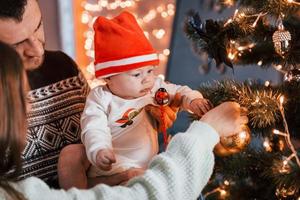 père et mère avec leur enfant décorant un arbre ensemble dans la chambre photo