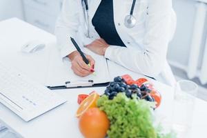 nutritionniste féminine en blouse blanche assise à l'intérieur au bureau sur le lieu de travail photo