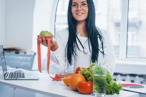 nutritionniste féminine en blouse blanche assise à l'intérieur au bureau sur le lieu de travail photo