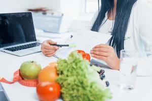 nutritionniste féminine en blouse blanche assise à l'intérieur au bureau sur le lieu de travail photo