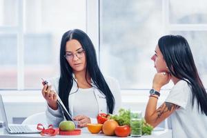 une nutritionniste avec un ordinateur portable donne une consultation au patient à l'intérieur du bureau photo