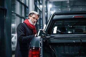 vieil homme à la mode avec des cheveux gris et une moustache à la recherche d'une nouvelle voiture à l'intérieur dans le salon photo