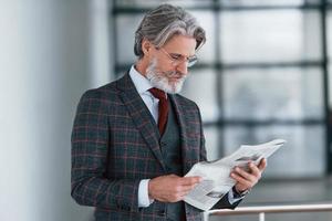 homme d'affaires senior en costume et cravate aux cheveux gris et à la barbe tient le journal dans les mains photo