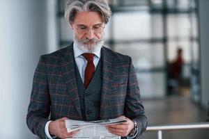 homme d'affaires senior en costume et cravate aux cheveux gris et à la barbe tient le journal dans les mains photo