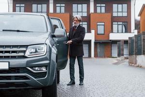 homme senior à la mode aux cheveux gris et à la barbe ouvrant la porte de sa voiture à l'extérieur dans la rue photo