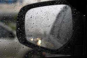 goutte de pluie sur la vitre de la voiture. flou de l'aile du miroir avec la lumière des phares de la voiture qui a clignoté deux fois. photo