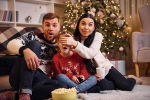 famille heureuse à l'intérieur dans une salle décorée de noël célébrant le nouvel an avec du pop-corn photo