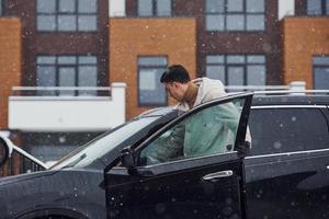 jeune bel homme à l'extérieur près de sa voiture noire moderne à l'heure d'hiver photo