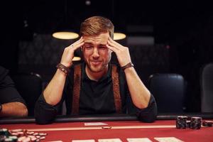 un jeune homme élégant est assis dans un casino et se sent mal parce qu'il perd une partie de poker photo