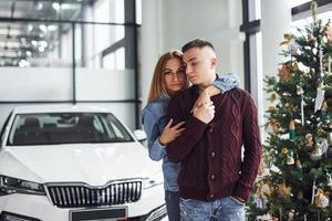 beau couple debout près de la voiture et de l'arbre de noël au moment du nouvel an photo