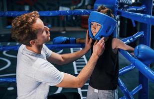 un jeune entraîneur de boxe aide un petit garçon à porter des vêtements de protection sur le ring entre les rounds photo