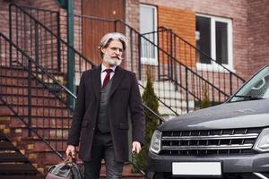 homme âgé à la mode avec des cheveux gris et une barbe est à l'extérieur dans la rue près de sa voiture photo