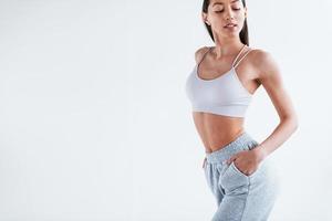 jeune femme en vêtements sportifs et avec une belle forme de corps debout dans le studio sur fond blanc photo