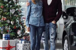 vue rapprochée d'un couple adorable qui se tient près de la voiture et de l'arbre de noël au moment du nouvel an photo