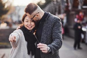 avec des cierges magiques dans les mains. heureux couple multiracial ensemble à l'extérieur de la ville photo