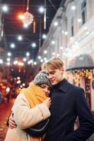 jeune couple positif dans des vêtements chauds s'embrassant sur la rue décorée de noël photo