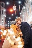 jeune couple dans des vêtements chauds s'embrassant sur la rue décorée de noël photo