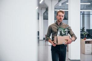 employé de bureau en tenue de soirée marchant avec une boîte avec une plante verte à l'intérieur photo