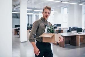 employé de bureau en tenue de soirée marchant avec une boîte avec une plante verte à l'intérieur photo