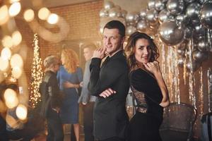 jeune couple debout ensemble contre leurs amis dans une salle décorée de noël et célébrant le nouvel an photo