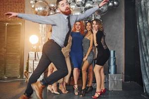 jeunes femmes en vêtements de fête debout à l'intérieur de la salle décorée de noël ensemble et regarde l'homme qui s'amuse à faire des tours photo