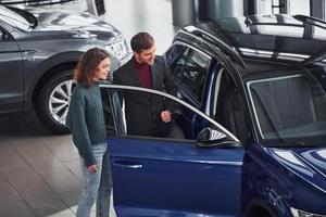 vendeur professionnel aidant une jeune fille en choisissant une nouvelle automobile moderne à l'intérieur photo