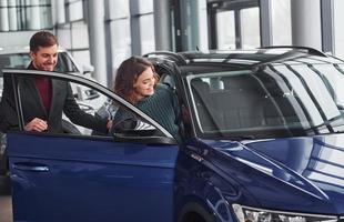 vendeur professionnel aidant une jeune fille en choisissant une nouvelle automobile moderne à l'intérieur photo