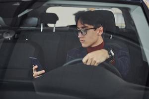 homme en lunettes et vêtements formels assis à l'intérieur d'une voiture moderne photo