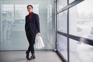 avec des sacs à provisions. jeune homme d'affaires en costume de luxe et vêtements formels est à l'intérieur du bureau photo