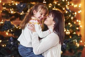 mère embrassant sa petite fille dans une chambre décorée de noël photo