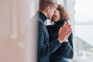 joli jeune couple s'embrassant à l'intérieur près de la fenêtre photo