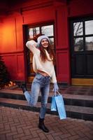 une jeune fille en vêtements chauds se promène à l'extérieur de la ville le soir près d'un bâtiment avec des lumières festives artificielles. tenant des sacs à provisions photo