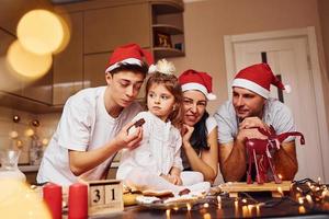 la famille festive en chapeaux de noël s'amuse dans la cuisine et prépare la nourriture photo