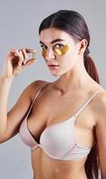 jeune femme en soutien-gorge dans le studio avec des bandes dorées près des yeux et avec une pilule à la main photo