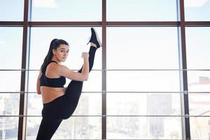 brune s'appuyant sur les balustrades de la fenêtre et faisant de longs étirements pour les jambes photo