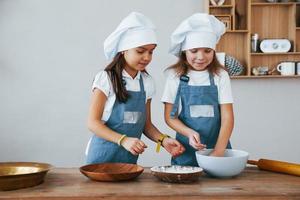 deux petites filles en uniforme de chef bleu travaillant avec de la farine dans la cuisine photo