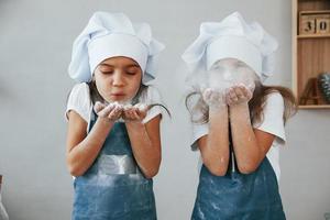 deux petites filles en uniforme de chef bleu soufflent la farine des mains sur la cuisine photo