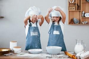 deux petites filles en uniforme de chef bleu travaillant avec de la farine dans la cuisine photo