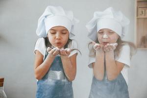 deux petites filles en uniforme de chef bleu soufflent la farine des mains sur la cuisine photo