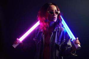 portrait de jeune fille à lunettes tenant des bâtons lumineux en néon rouge et bleu en studio photo