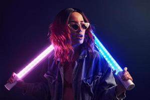 portrait de jeune fille à lunettes tenant des bâtons lumineux en néon rouge et bleu en studio photo