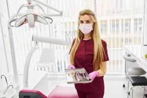 jeune femme dentiste en uniforme debout dans le bureau de stomatologie avec des outils dans les mains photo