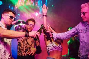 célébrer et frapper des bouteilles avec de l'alcool. les jeunes s'amusent dans une boîte de nuit avec des lumières laser colorées photo