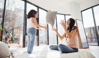 s'amuser avec un oreiller sur le lit. jeune mère avec sa fille passant le week-end ensemble dans la chambre photo