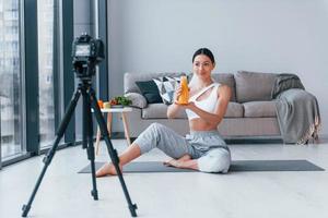 blogueuse jeune femme au corps mince en vêtements de sport parlant de légumes, de fruits et d'aliments sains à l'intérieur à la maison photo