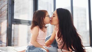 jeune mère avec sa fille passant le week-end ensemble dans la chambre et donnant un baiser photo