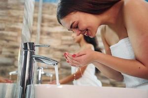 deux belles jeunes femmes debout dans la salle de bain près du miroir ensemble et se nettoyant le visage photo