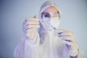 tient la seringue. portrait d'une femme médecin scientifique en blouse de laboratoire, lunettes défensives et masque photo