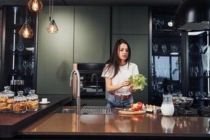 jeune belle brune en vêtements décontractés préparant des aliments sains dans la cuisine pendant la journée photo