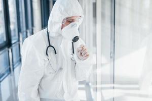 se sent mal et malade. femme médecin scientifique en blouse de laboratoire, lunettes défensives et masque debout à l'intérieur photo